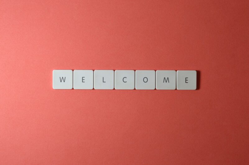 The image shows seven white square tiles arranged in a horizontal line on a red background. Each tile has a single black letter, collectively spelling out the word "WELCOME".
